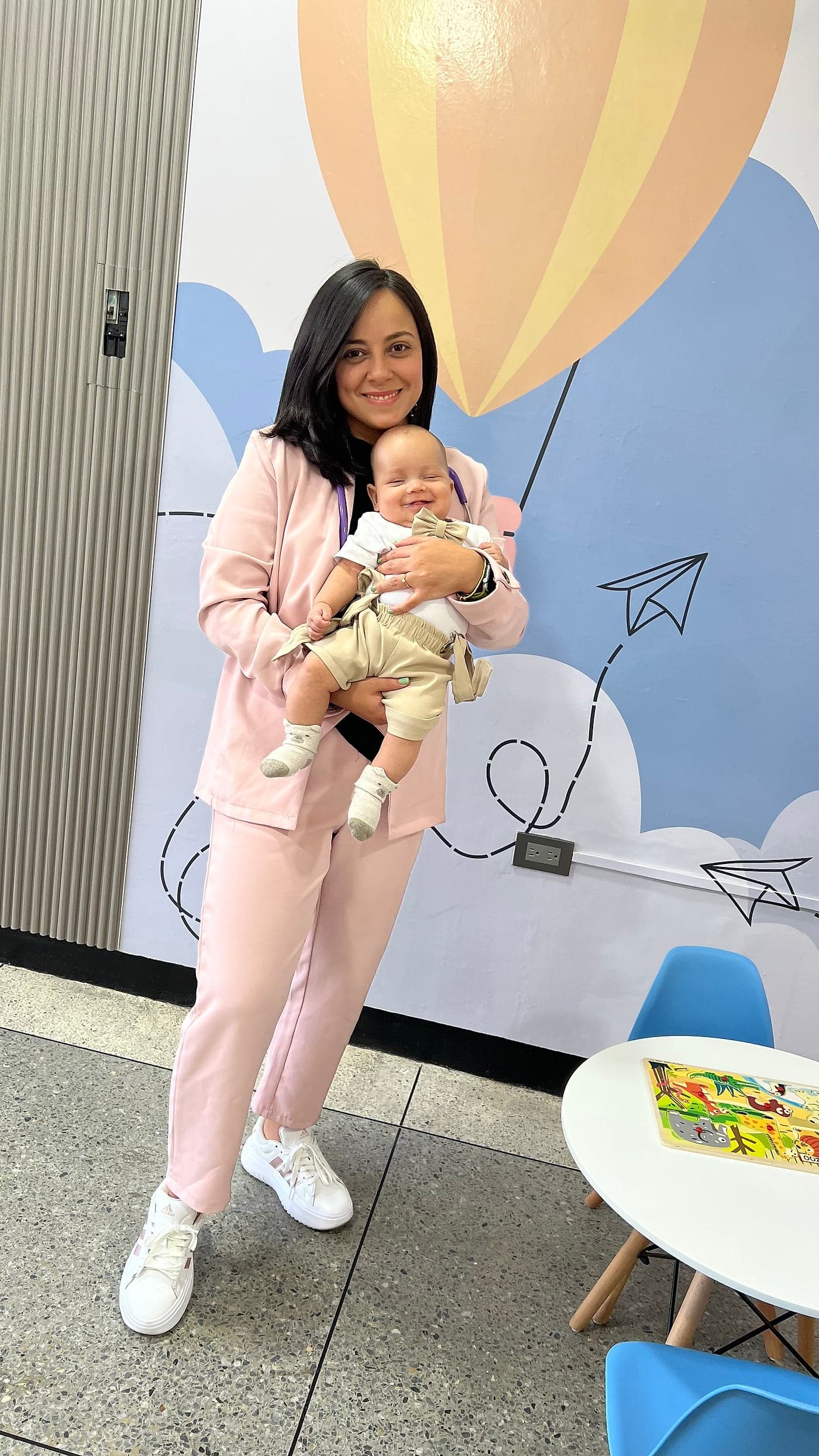 La Dra. Gretzalid Meléndez con un bebé en brazos, frente al mural de la consulta